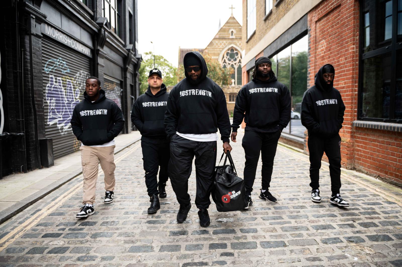 Five individuals wearing black hoodies with '10 strength' branding on a street.