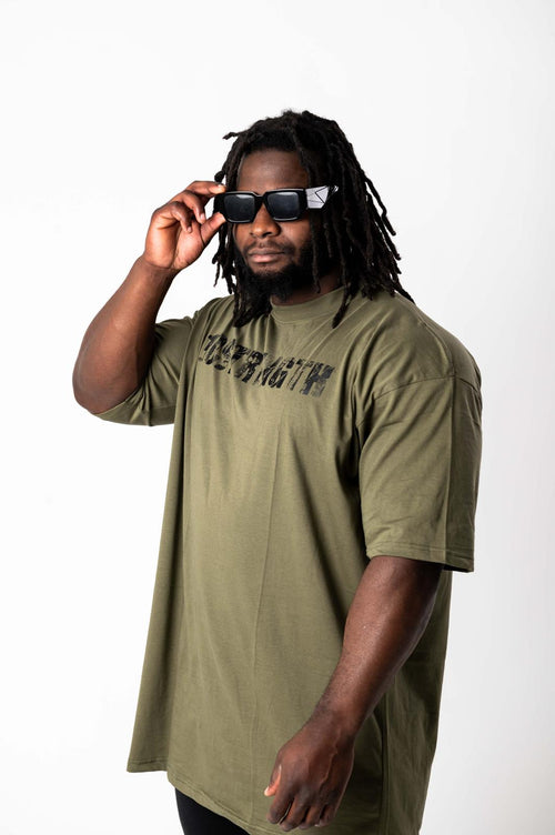 Man wearing an olive green t-shirt with text, holding sunglasses, on a white background
