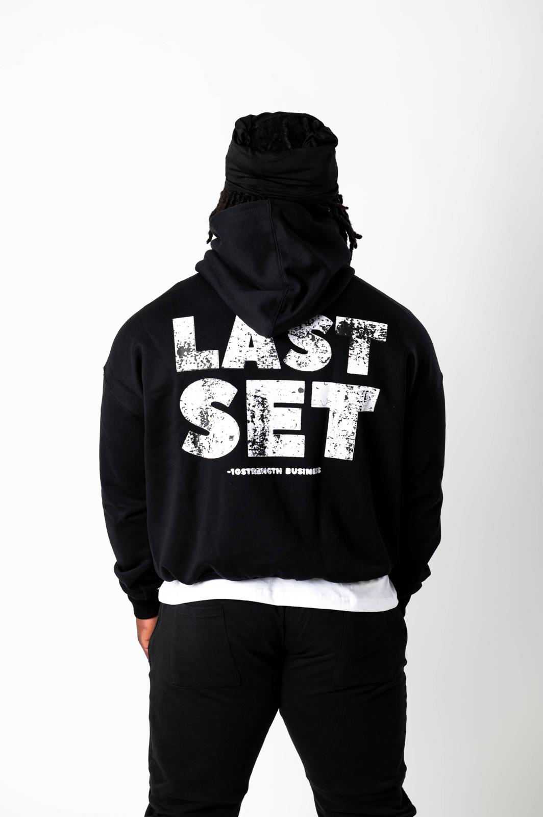 Person wearing a black hoodie with 'LAST SET' text on the back against a white background