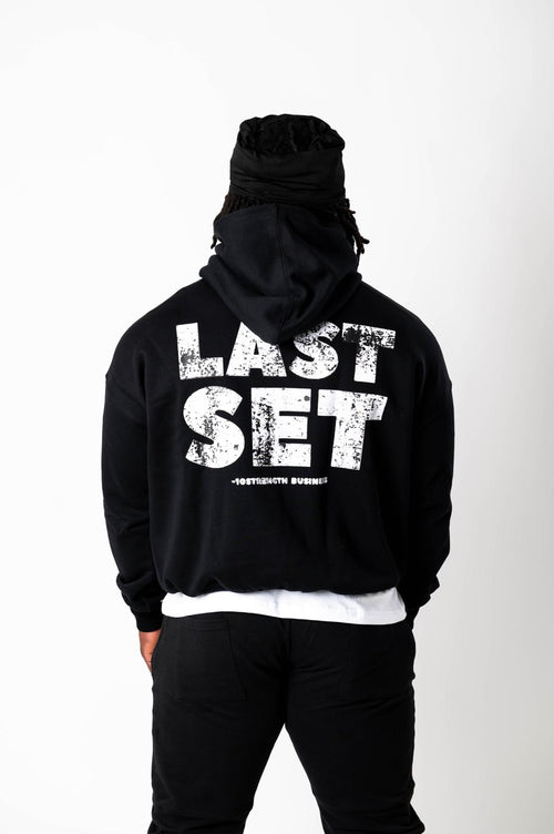 Person wearing a black hoodie with 'LAST SET' text on the back against a white background